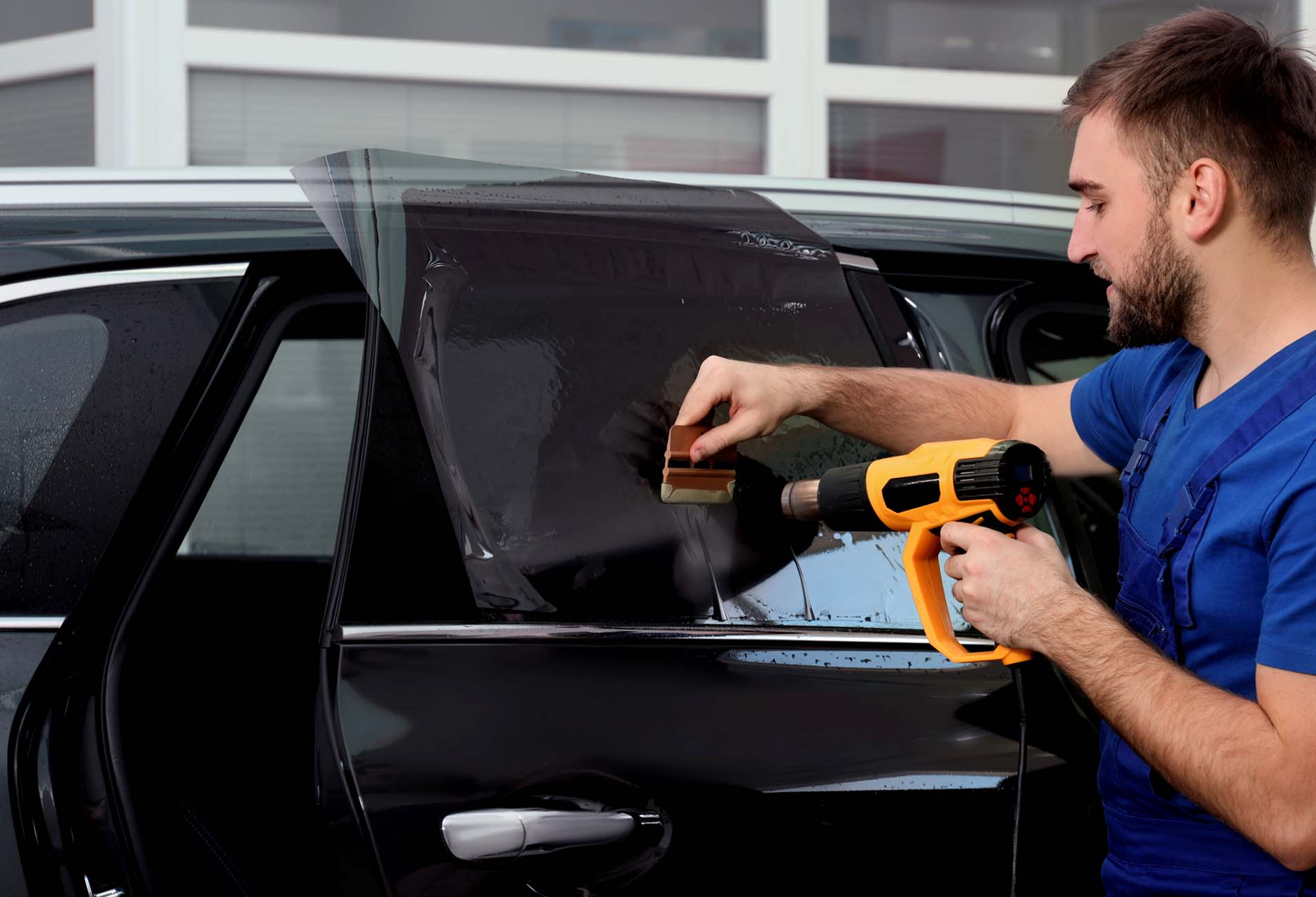 technician installing car window tint with heat gun