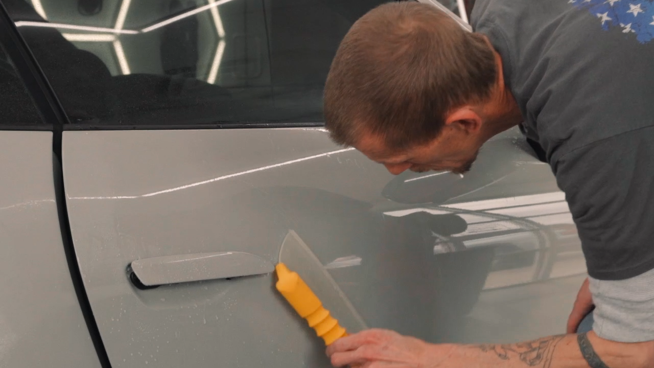 a man applying paint protection film on grey car door
